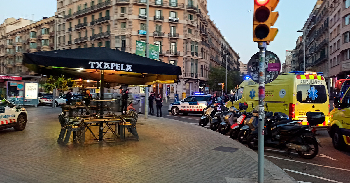 Una de las dos personas involucradas en la pelea (centro) sentada en una acera de la plaza de Cataluña acompañada de los Mossos d'Esquadra / HUGO SÁNCHEZ