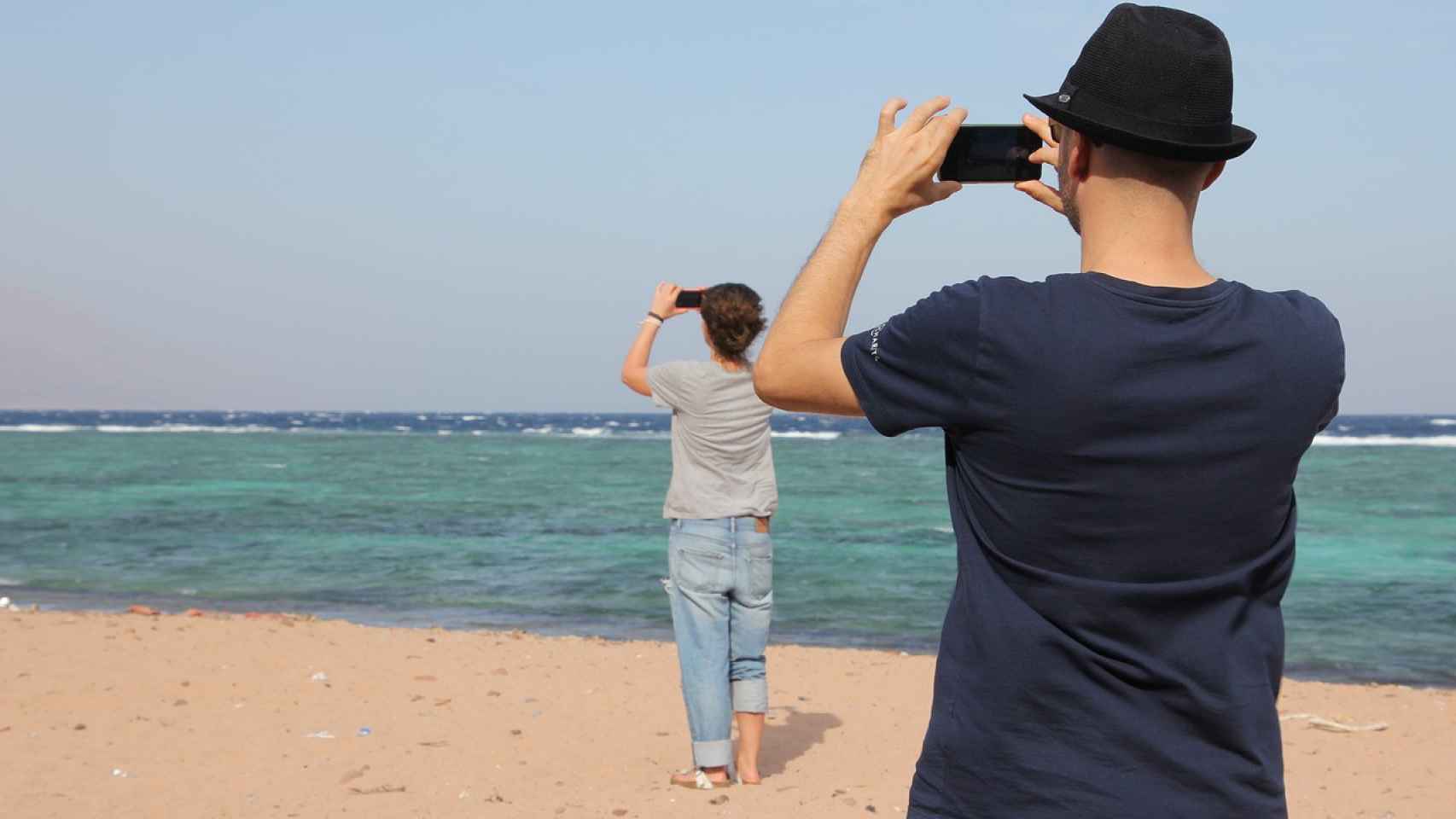 Dos personas utilizando el móvil en una playa / CG