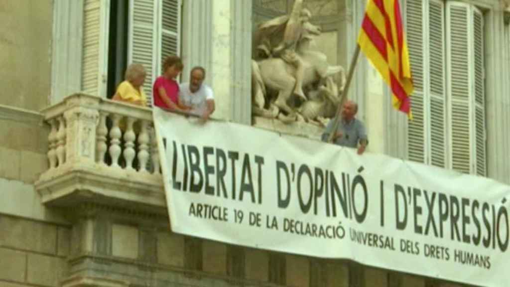 Lluís Llach (d), Antoni Baños (2 d) y Sílvia Bel (2 i) cuelgan una pancarta a favor de la libertad de opinión y expresión en el Palau de la Generalitat