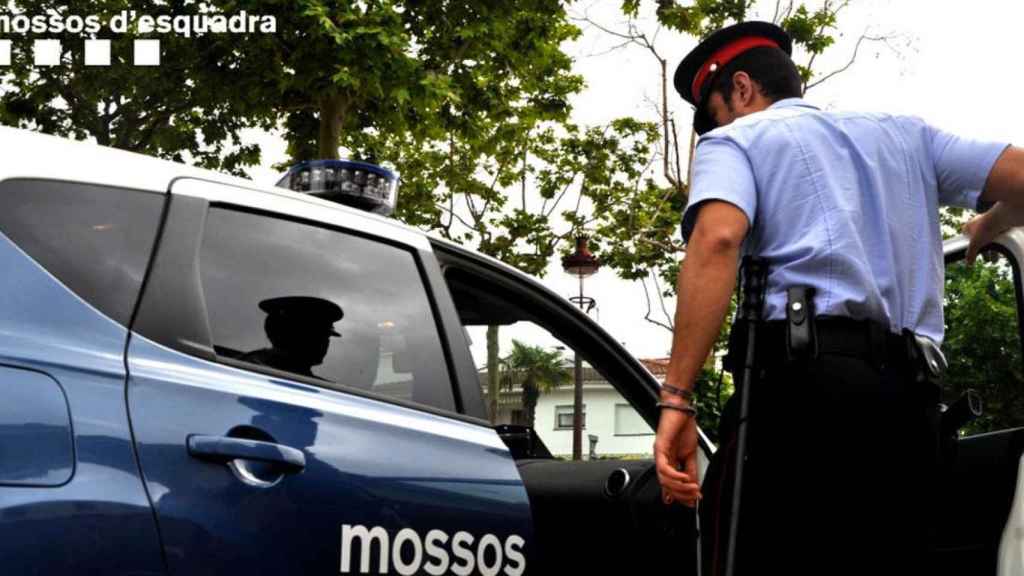 Un mosso entra a su coche patrulla donde hay un detenido / MOSSOS