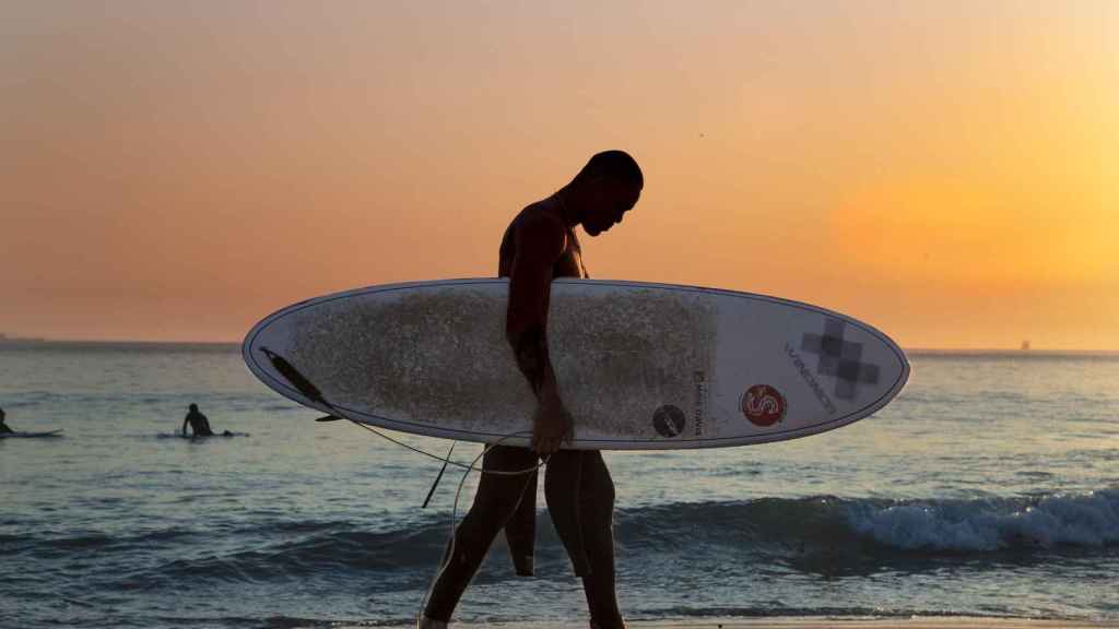 Un surfista abandona una playa al atardecer / CG