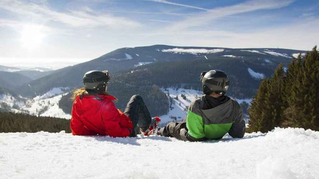 Pareja descansando en la nieve tras practicar esquí / BOOKING