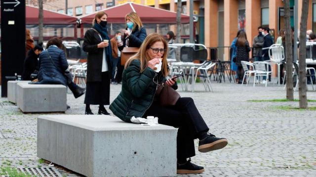 Una ciudadana desayuna en un banco ante la Ciudad de la Justicia por el cierre de los bares / EFE