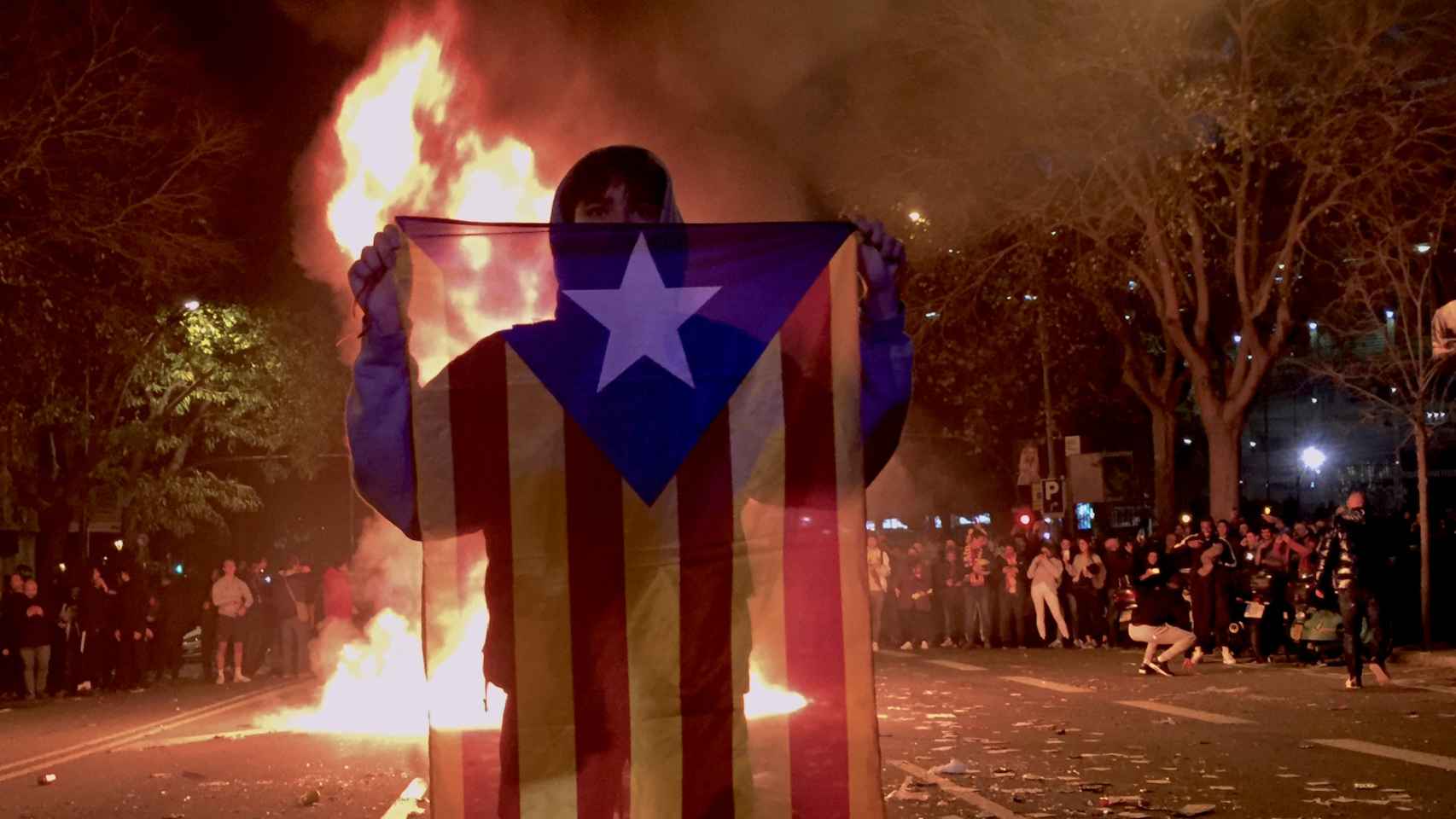 Un manifestante blande una bandera estelada frente a contenedores en llamas en los alrededores del Camp Nou / EB