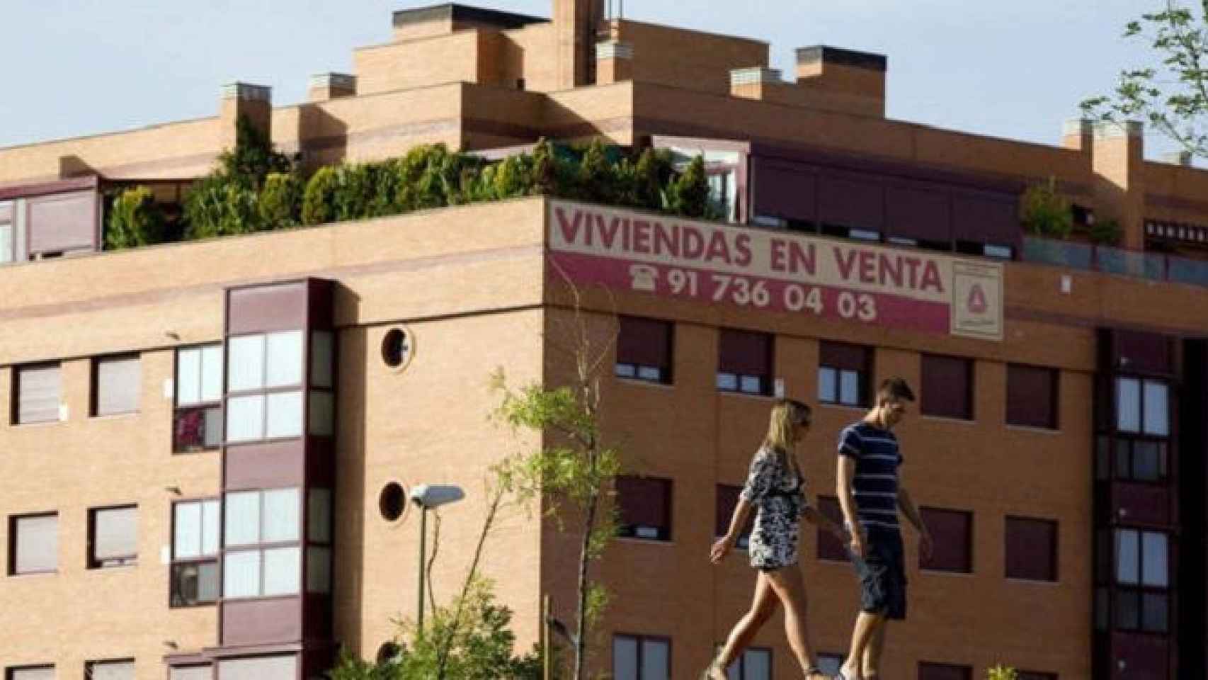 Una pareja pasa por delante de un bloque de pisos en venta / EFE