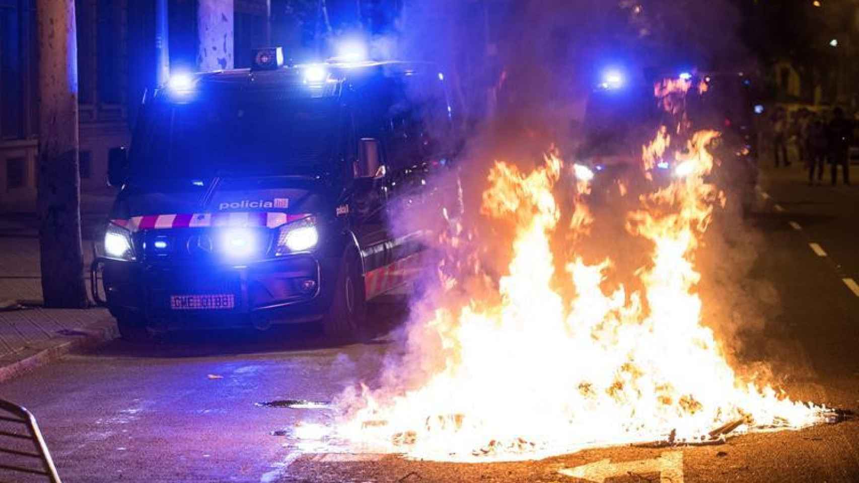 Una furgoneta de los Mossos d'Esquadra pasa junto a la hoguera hecha por los manifestantes / EFE