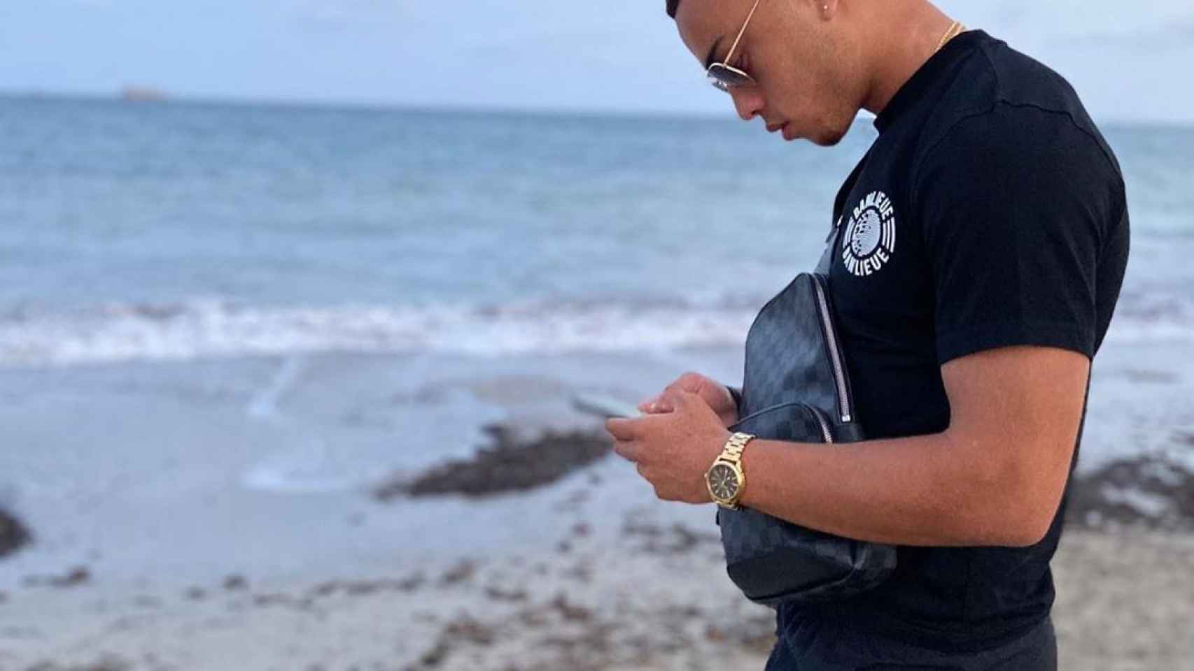 Sergiño Dest mirando el móvil en la playa