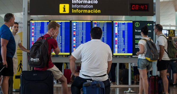 Imagen de dos pasajeros que observan la pantalla de horarios de los vuelos en el Aeropuerto de Barcelona-El Prat / EFE