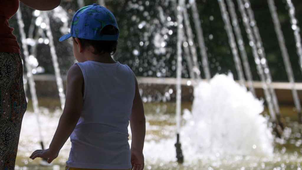 Niños y adultos se refrescan a la sombra, junto a las fuentes públicas del parque del Retiro en una jornada marcada por las altas temperaturas