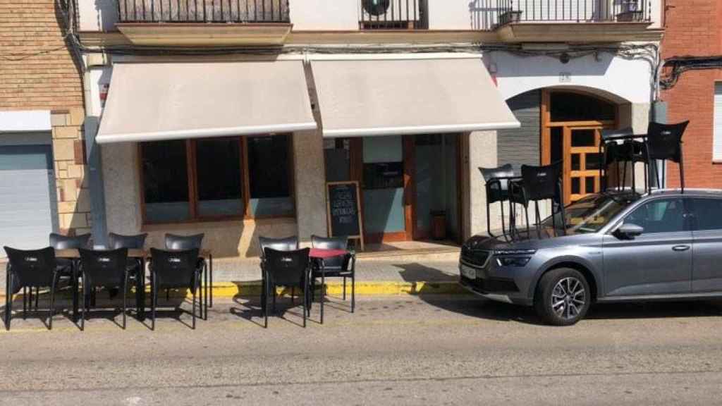 Un bar monta dos mesas de su terraza encima de un coche aparcado junto a la acera