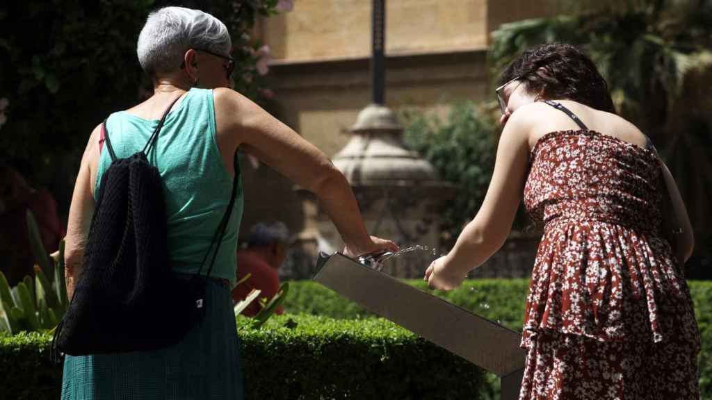 Dos mujeres beben agua de una fuente para combatir el calor