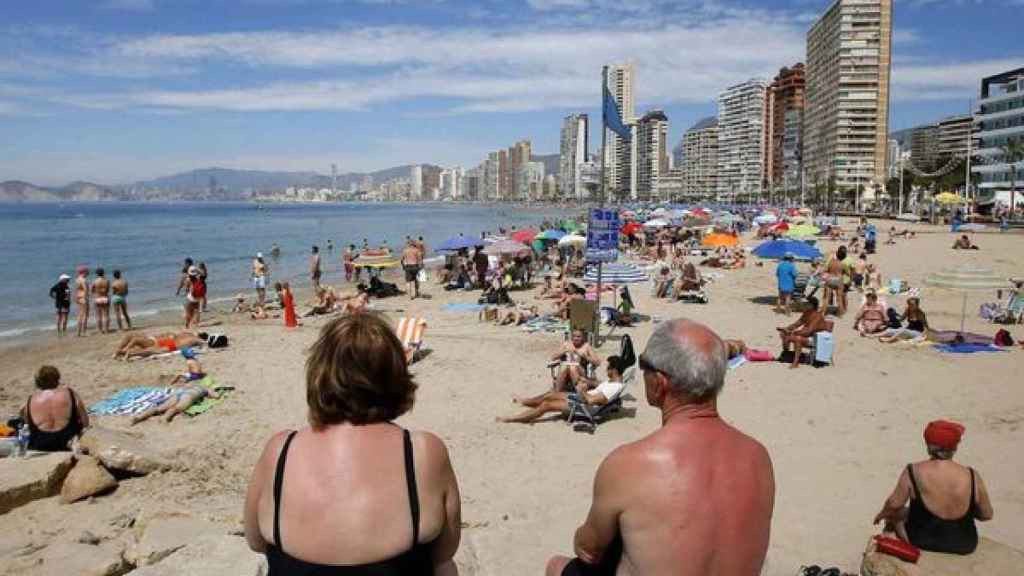 Dos personas mayores miran sentadas la línea de playa de Benidorm