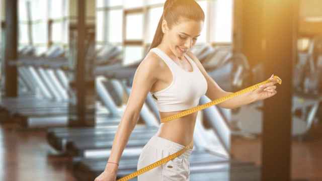 Mujer sonríe con cinta métrica en el gimnasio