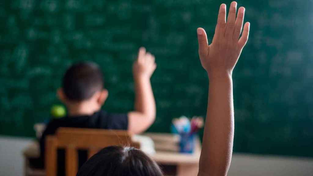 Dos alumnos levantan la mano en un aula