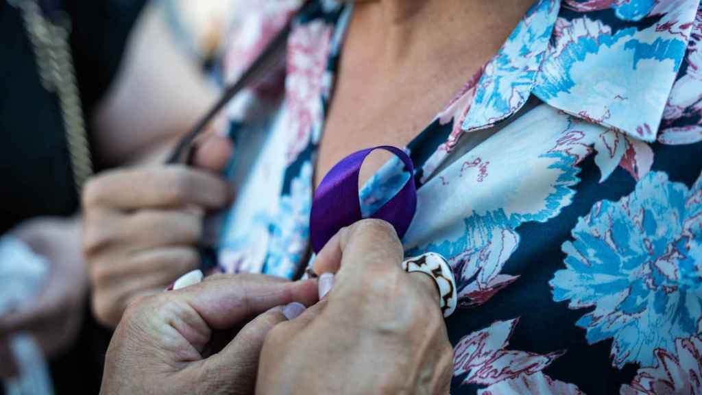 Una mujer pone un lazo morado a otra durante una concentración contra la violencia machista