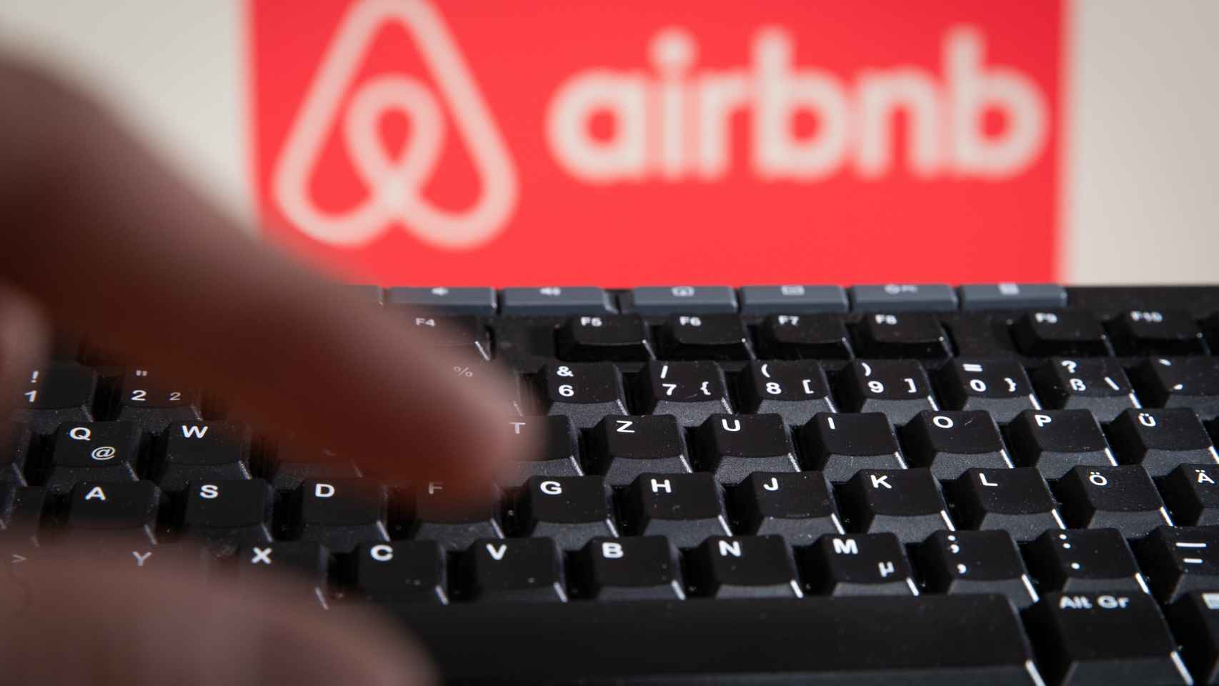 Un usuario consulta un ordenador con el logo de Airbnb de fondo