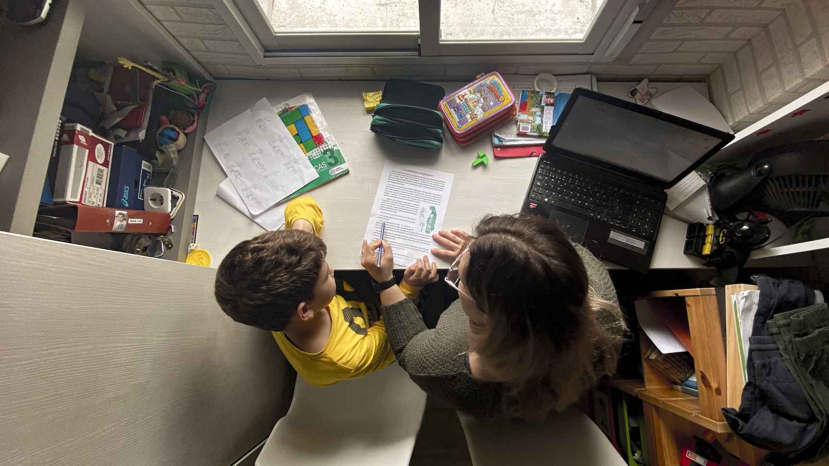 Un niño estudia y hace los deberes en casa con la ayuda de su madre
