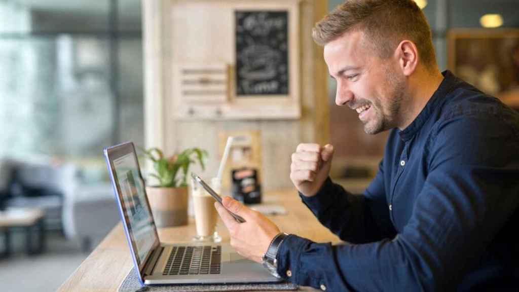 Un hombre usa feliz una aplicación frente a un portátil