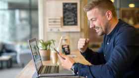 Un hombre usa feliz una aplicación frente a un portátil