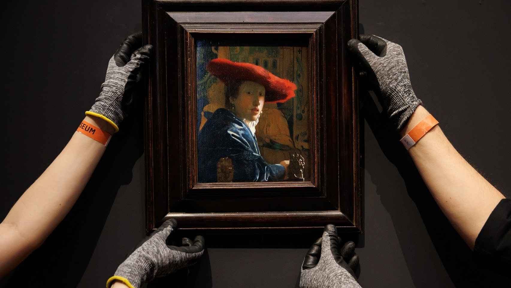 Dos operarios cuelgan la tabla Mujer con el sombrero rojo (1664-1667) en una de las salas del Rijksmuseum.