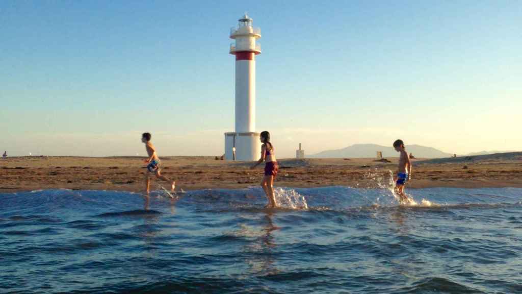 Unos niños juegan en la playa frente a un faro