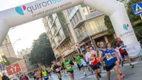 Corredores cruzan un arco publicitario de Quirónsalud durante una Media Maratón