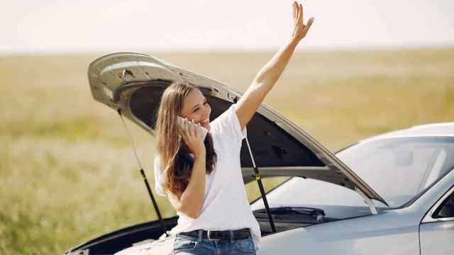 Una mujer saluda junto a su vehículo averiado