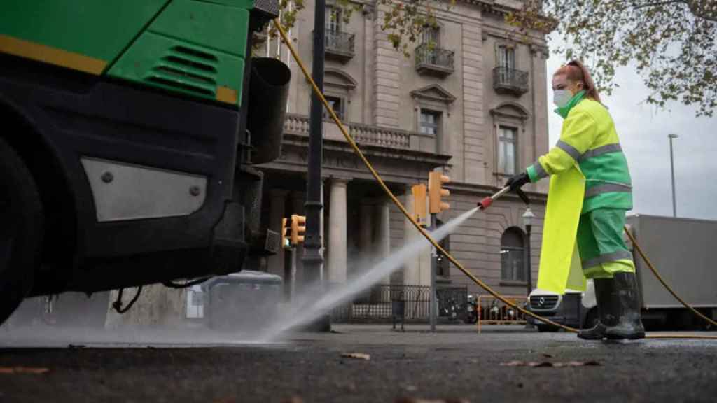 Una trabajadora riega una calle con una manguera en enero en Barcelona