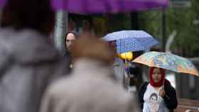 Varias personas con paraguas pasean por una de las calles de Barcelona