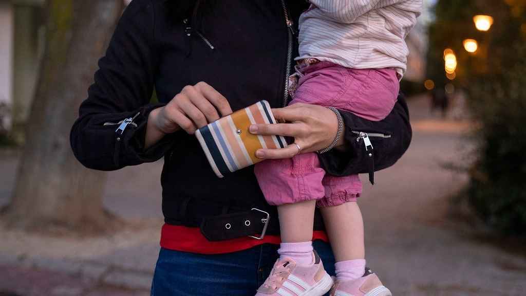 Una mujer mira el monedero mientras sositene un bebé