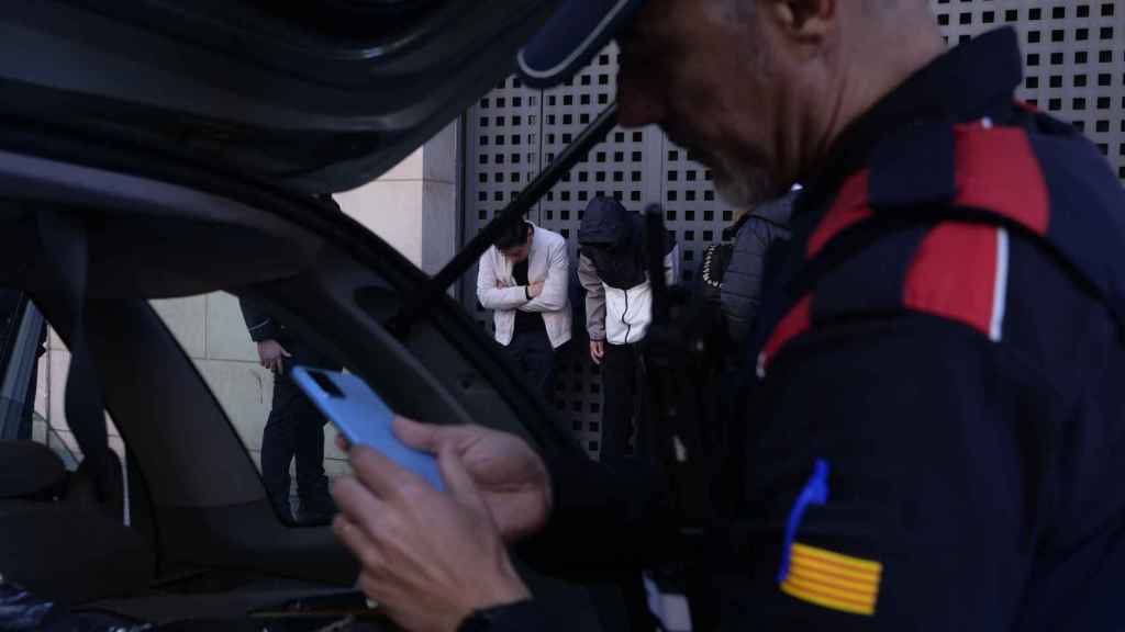 Agente de los Mossos revisando los teléfonos hurtados, con dos de los detenidos en el fondo