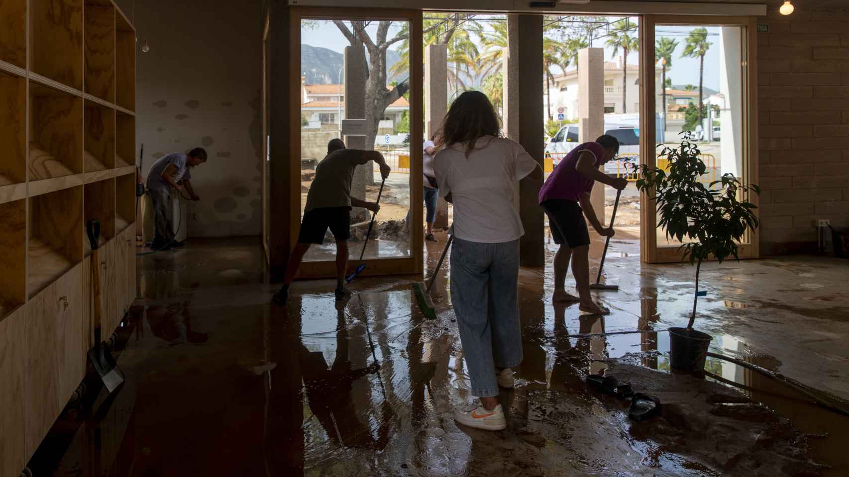 Varias personas limpian un negocio tras una inundación en Les Cases d'Alcanar (Tarragona), causada por las DANA de septiembre de 2023