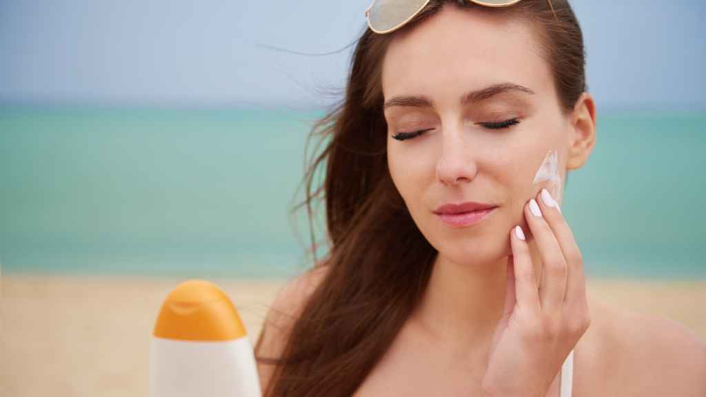 Una joven se extiende crema solar en el rostro para proteger su piel