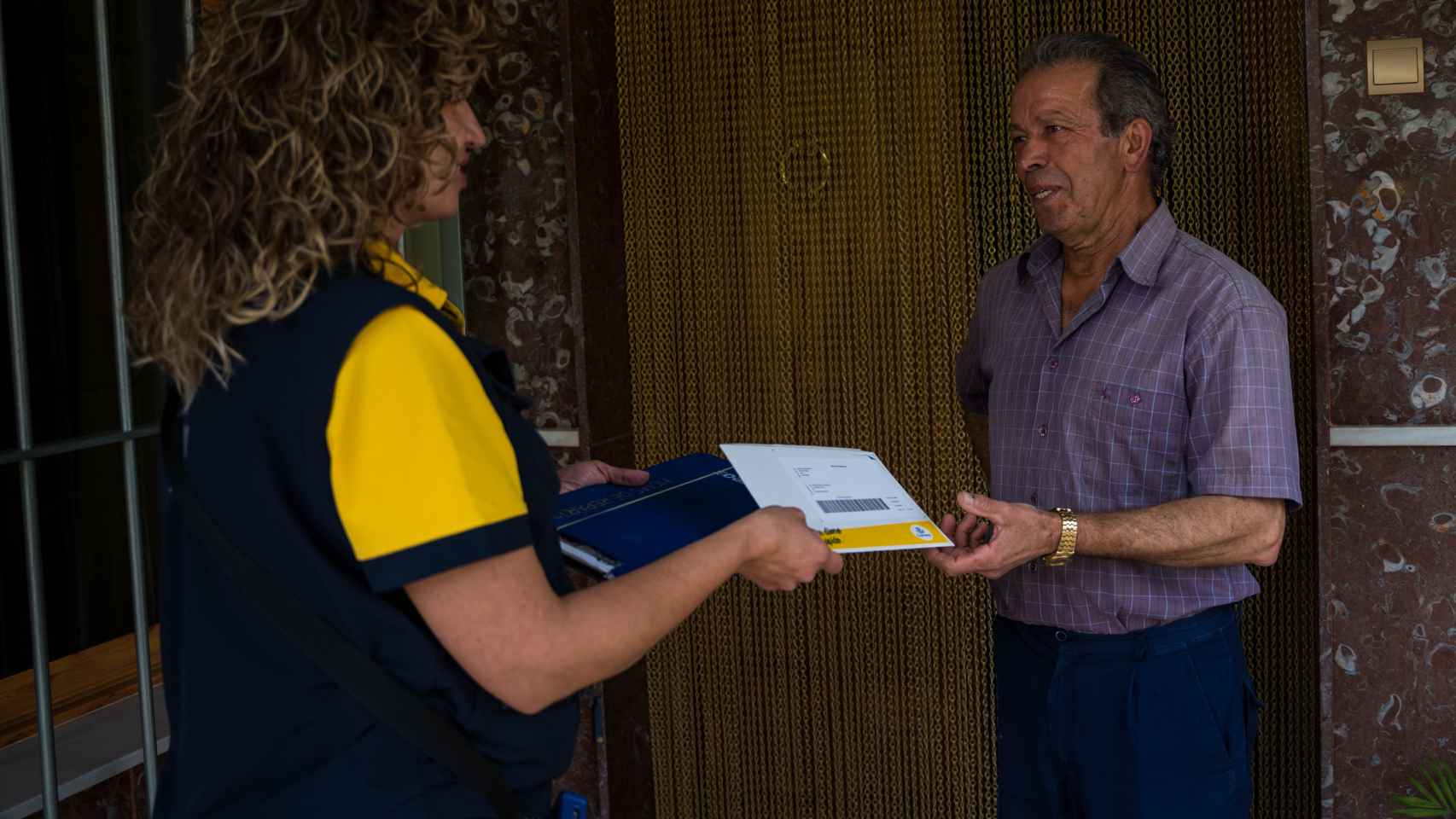 Una empleada de Correos entrega una carta a un hombre en la puerta de su domicilio