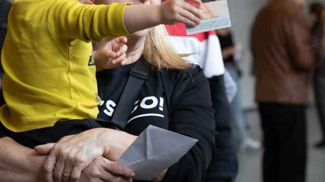 Una mujer sostiene a un menor en brazos con la documentación necesaria para votar en las elecciones del 12M