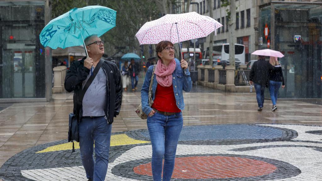 Varias personas se protegen de la lluvia mientras caminan por las Ramblas de Barcelona