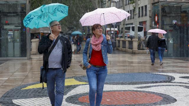 Varias personas se protegen de la lluvia mientras caminan por las Ramblas de Barcelona