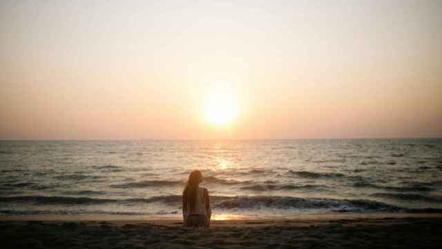 Chica en una playa paradisíaca contemplando el atardecer