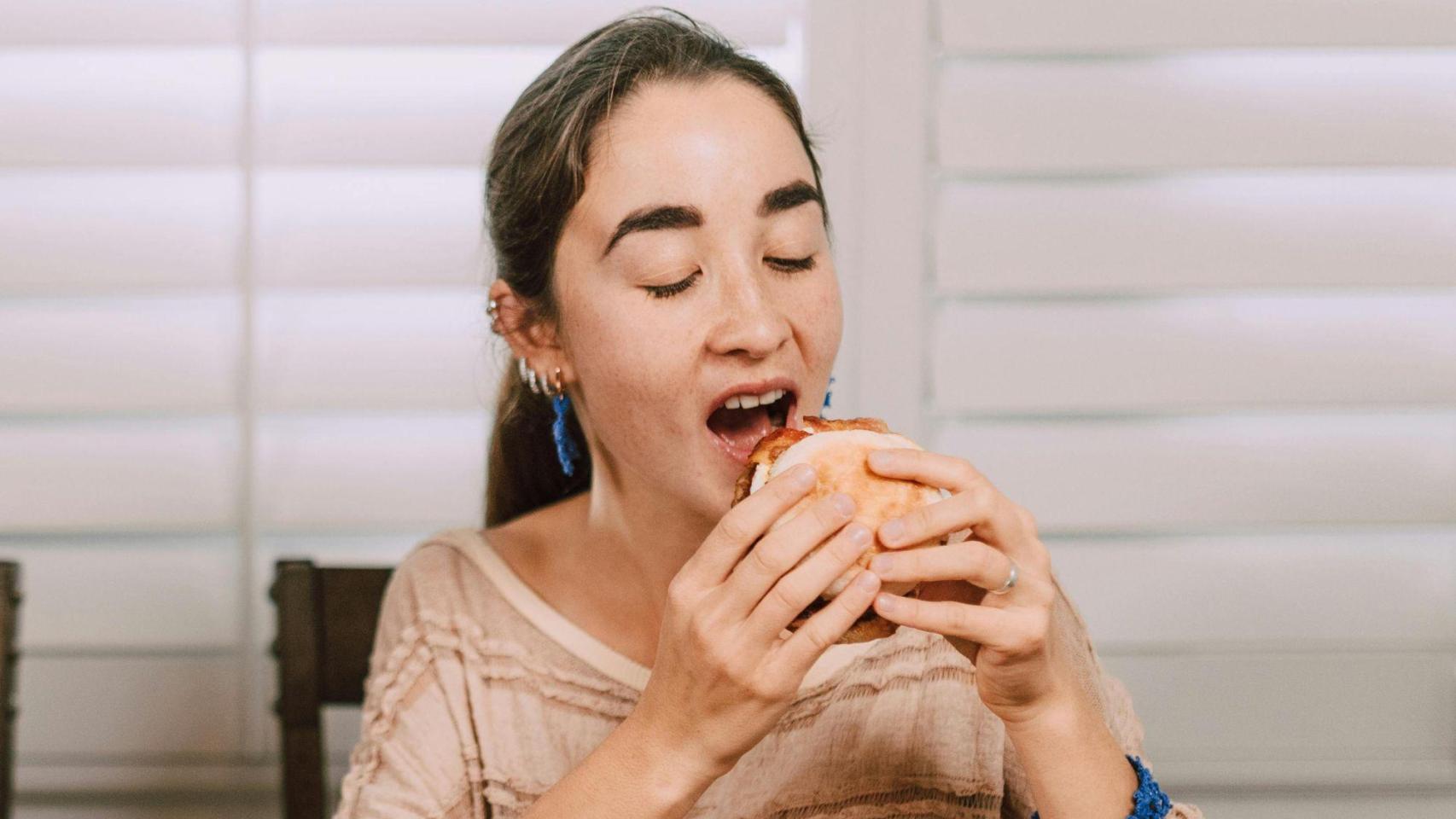 Una mujer comiendo un bocadillo | PEXELS