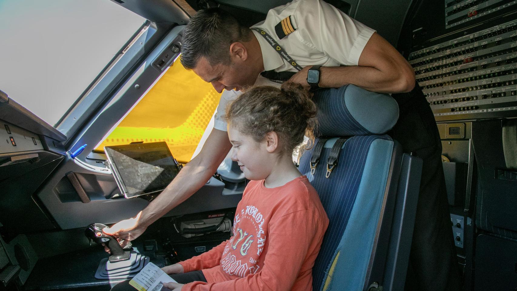 Un miembro de la tripulación de Vueling enseña la cabina a una niña