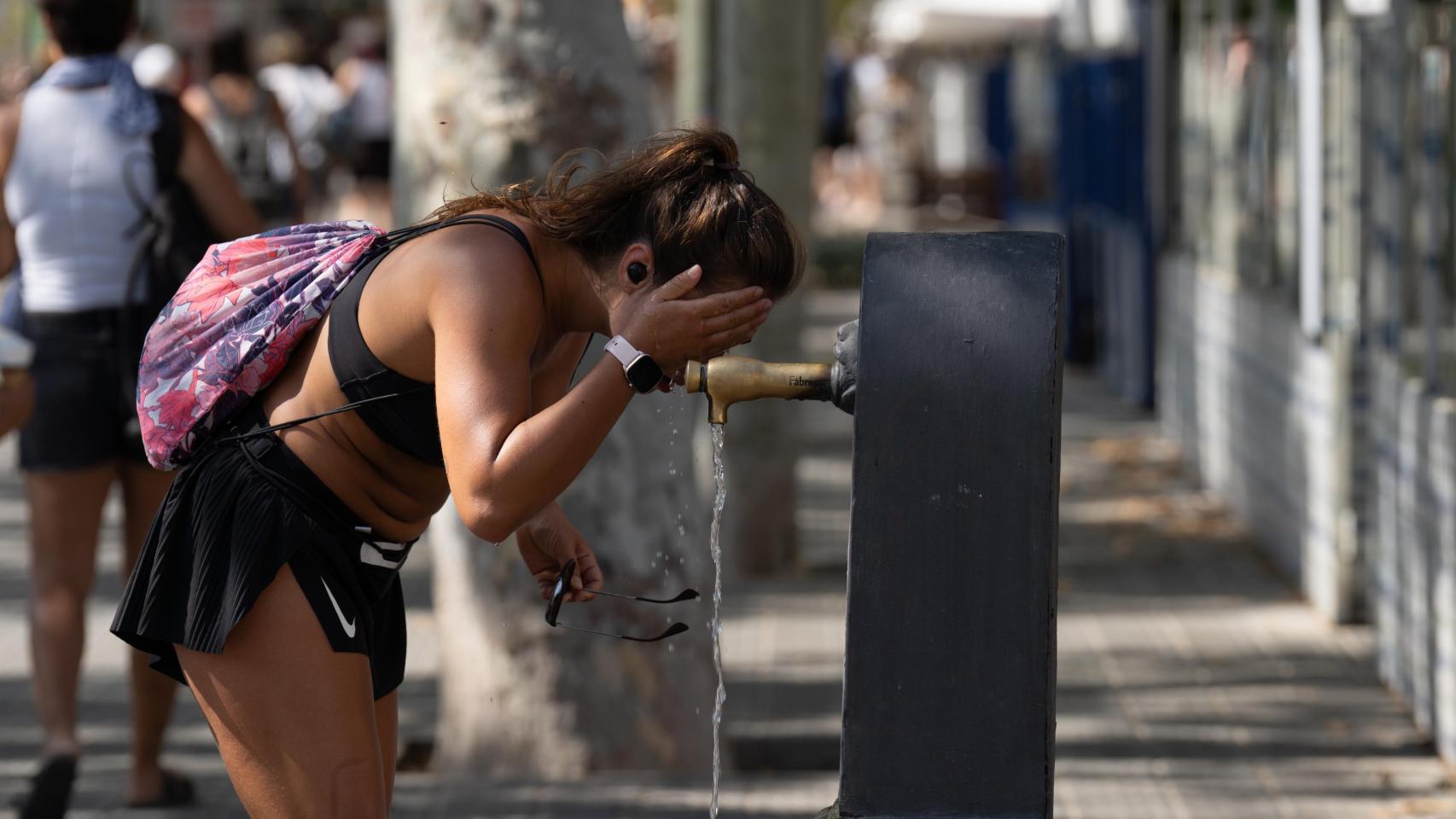 Una mujer se refresca en una fuente en Barcelona