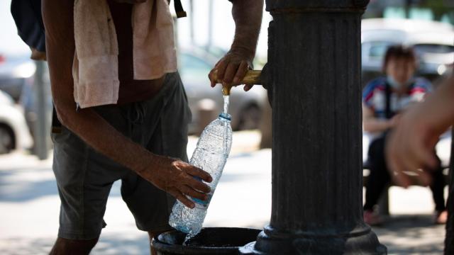 Un hombre rellena una botella de agua en una fuente en el parque de la Barceloneta, Barcelona, en pleno verano