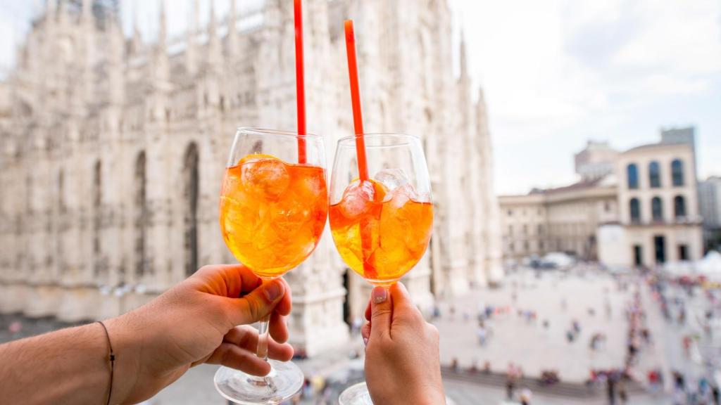 Dos personas brindando con Aperol Spritz frente al Duomo de Milán