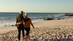 Una pareja de jubilados paseando por la playa | CANVA