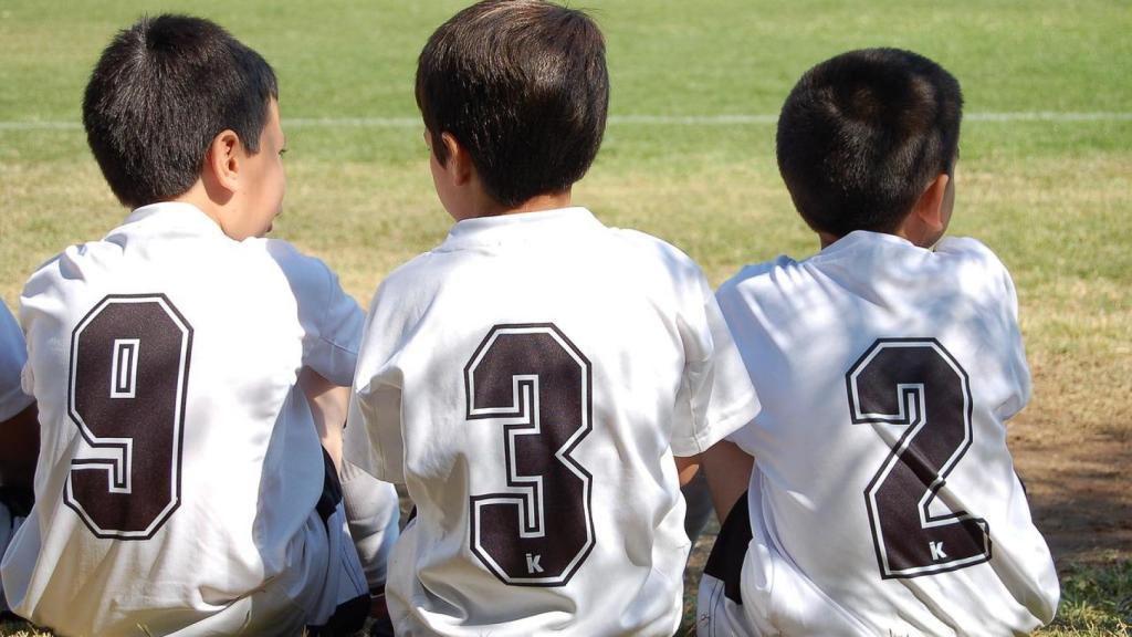 Imagen de archivo de tres niños sentados en el césped de un campo de fútbol