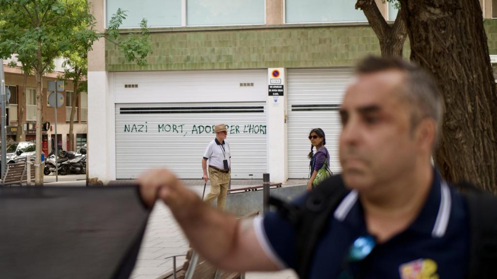 Militante de Democracia Nacional en el acto de Barcelona con un grafiti antifascista de fondo