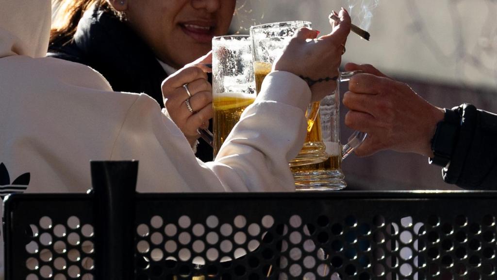 Una persona fumadora brinda con los ocupantes de la mesa de una terraza