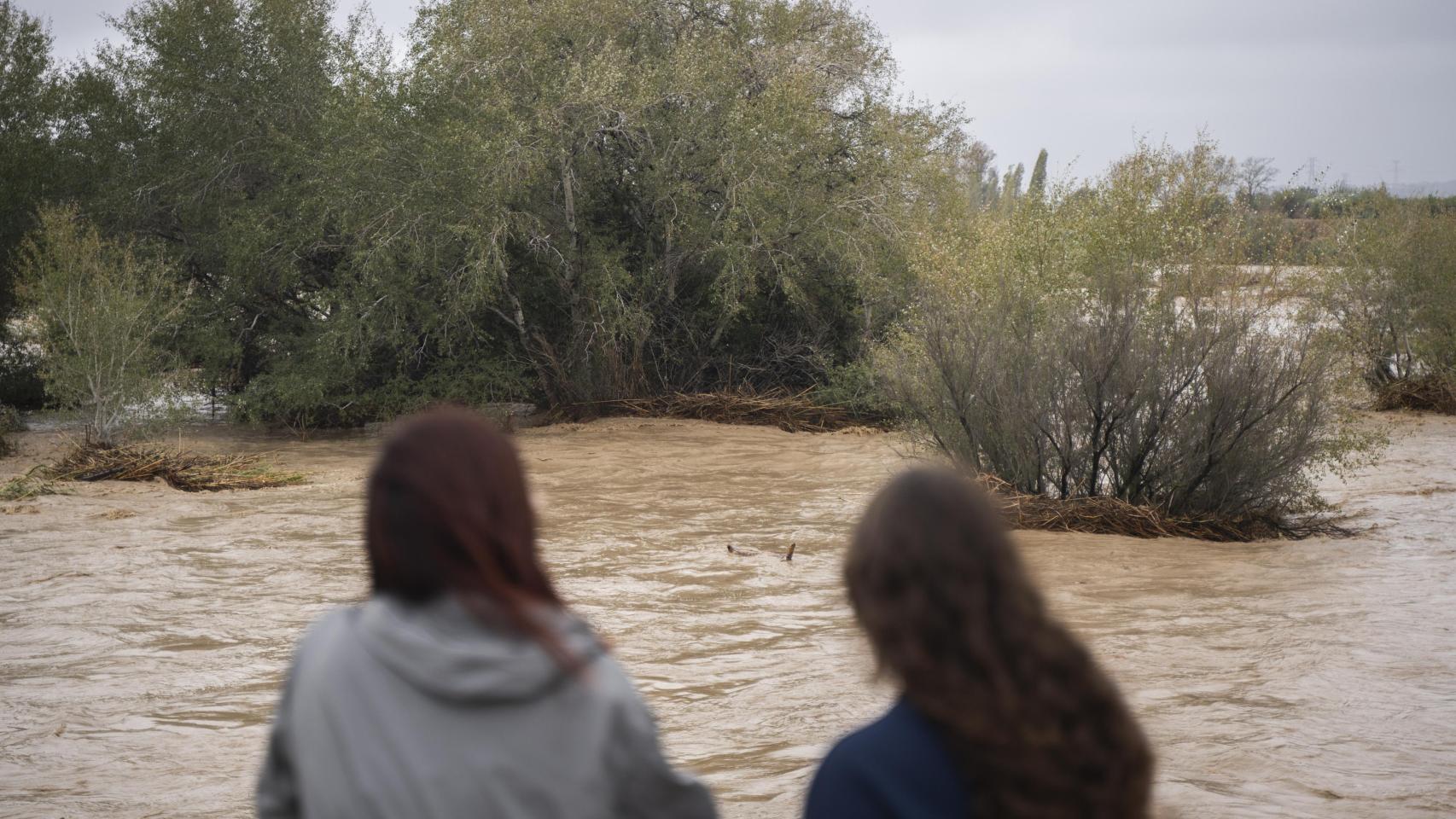 Varias personas observan la inundación por la crecida de un río por la DANA en Valencia