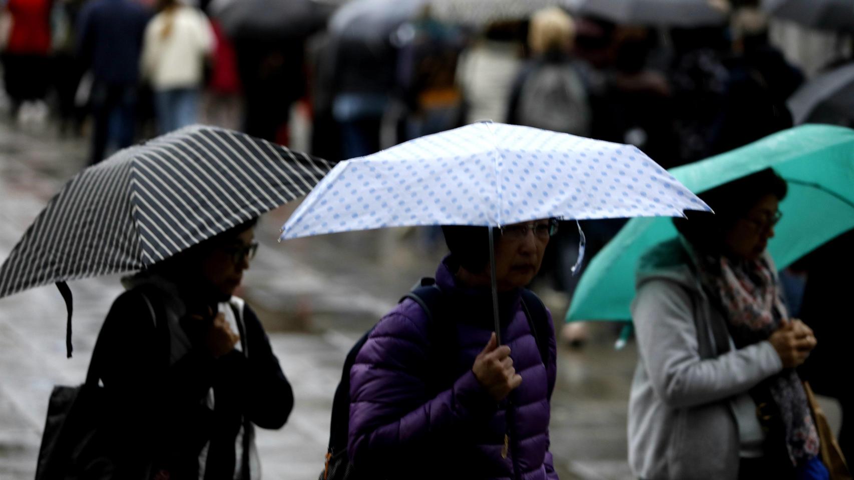 Varias personas se cubren de la lluvia con sus paraguas