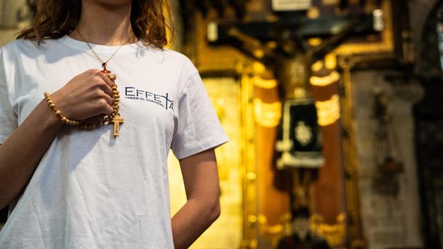 Una joven viste la camiseta de Effetá mientras sujeta un rosario en el interior de una iglesia católica